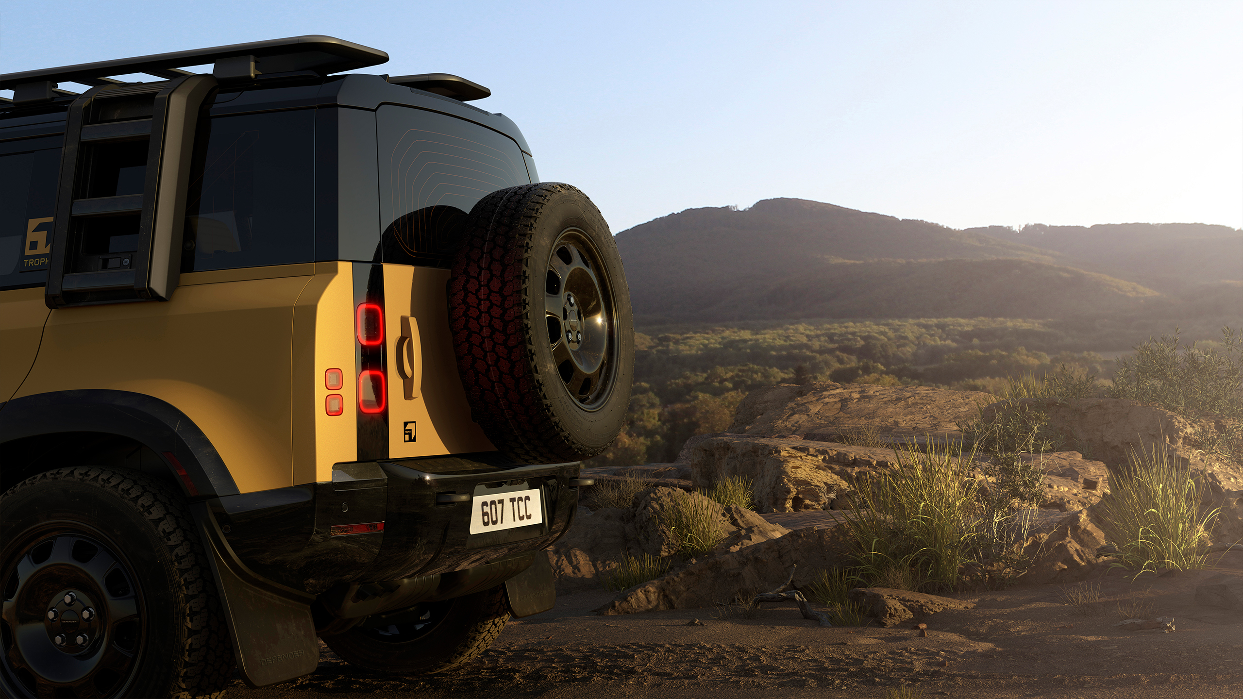 Rear view of a yellow Defender parked on a rocky landscape with hills in the background.